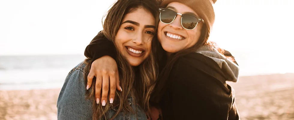 two women on a beach smiling and hugging